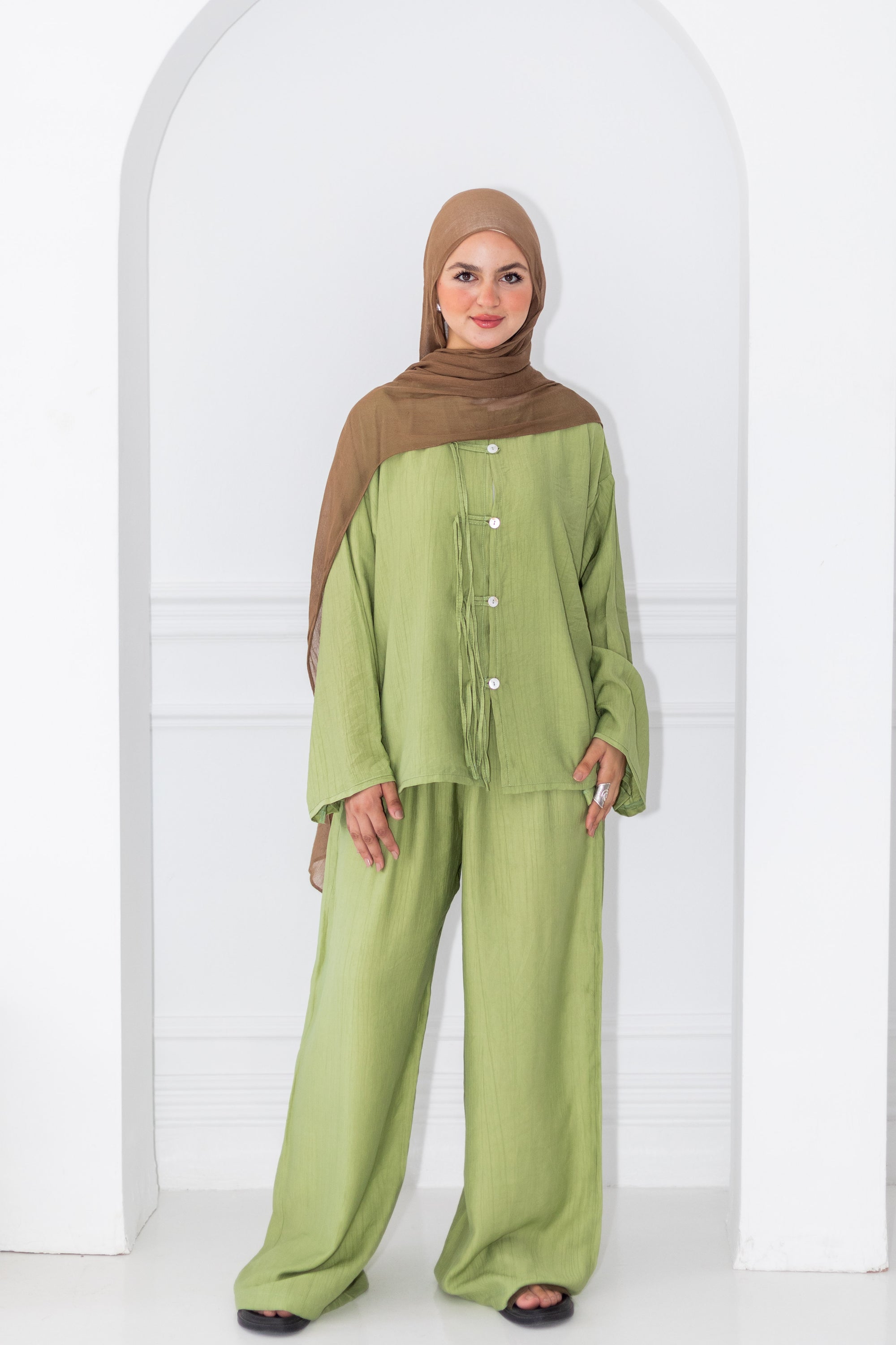 Woman wearing a green outfit with a brown hijab against a white background