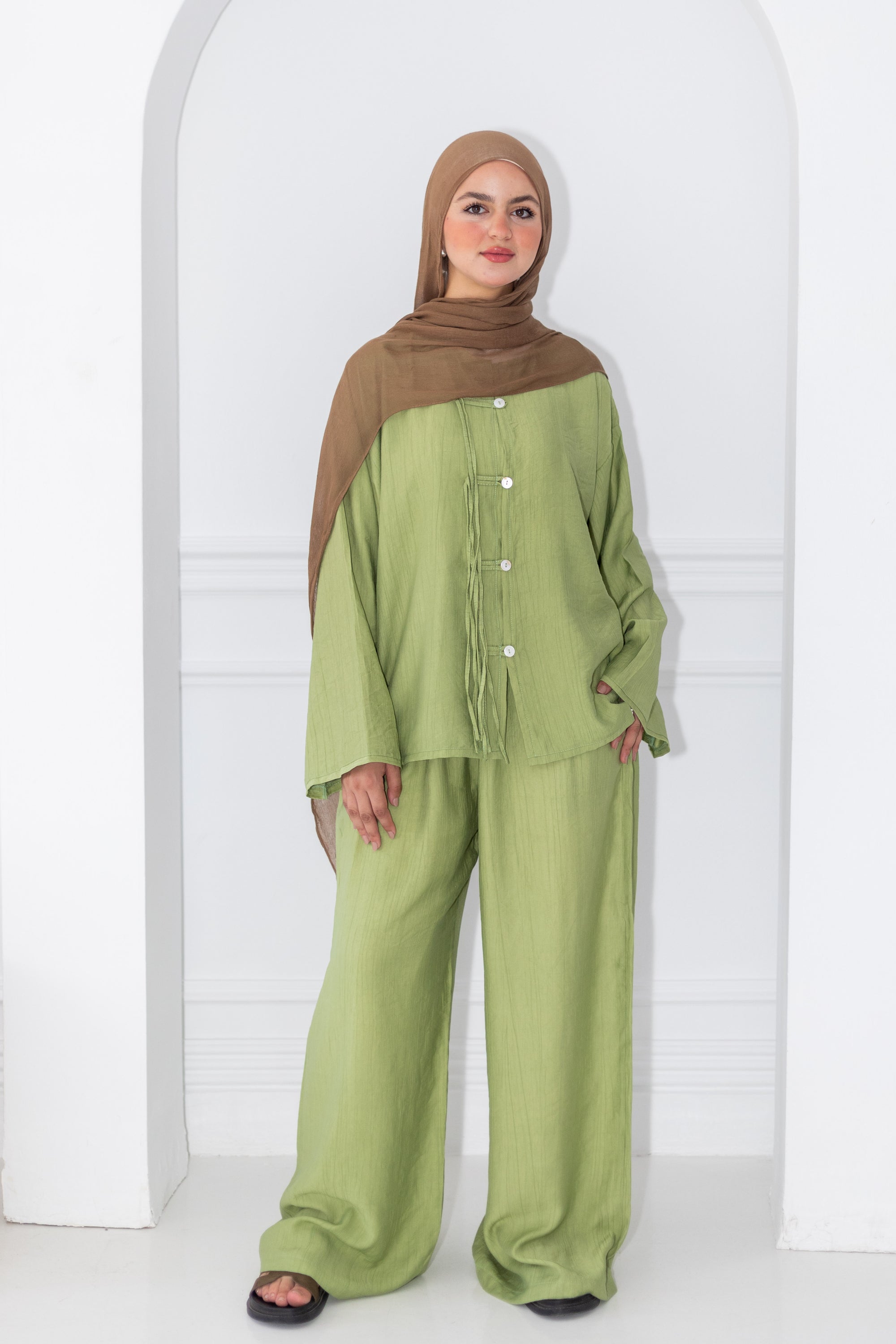 Woman wearing a green outfit with a brown hijab against a white background