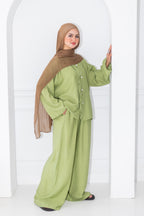 Woman wearing a green outfit with a brown hijab against a white background