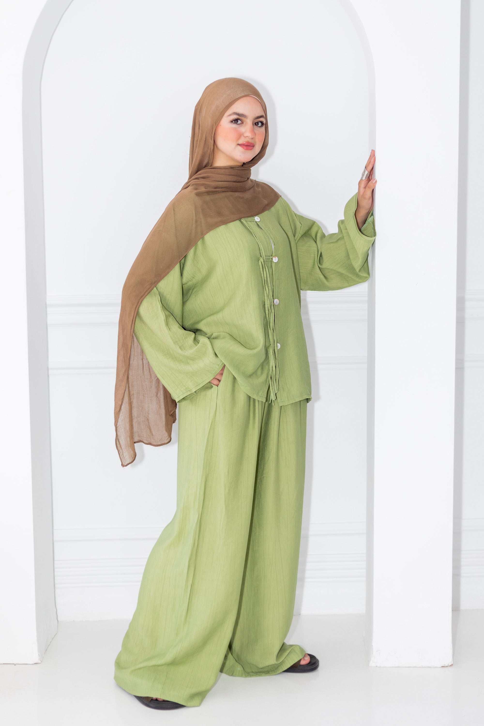Woman wearing a green outfit with a brown hijab against a white background