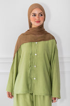 Woman wearing a green outfit with a brown hijab against a white background