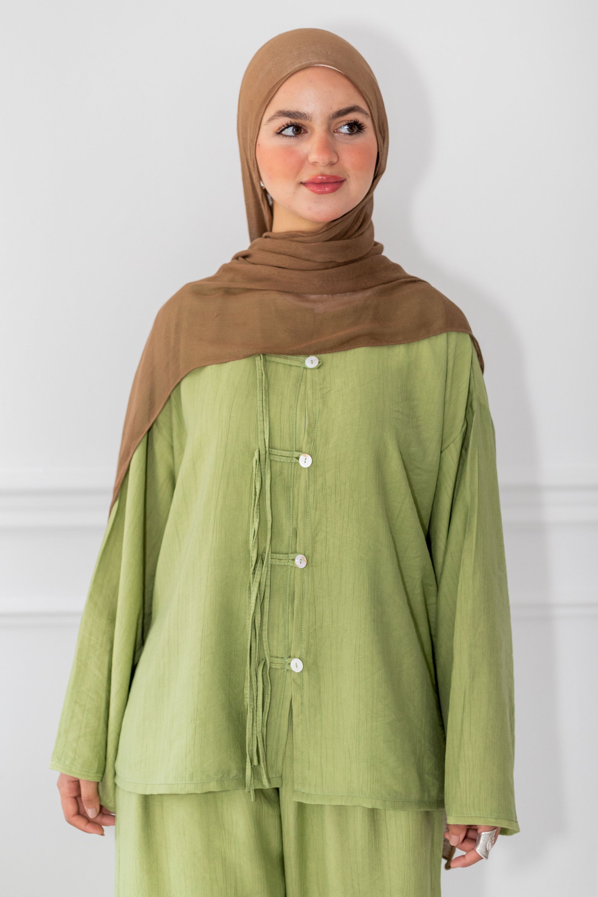 Woman wearing a green outfit with a brown hijab against a white background