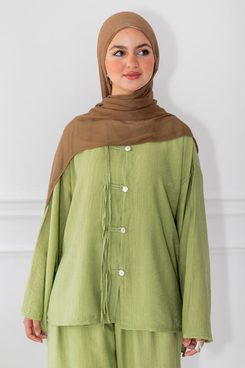 Woman wearing a green outfit with a brown hijab against a white background