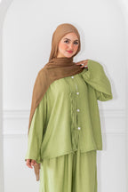 Woman wearing a green outfit with a brown hijab against a white background