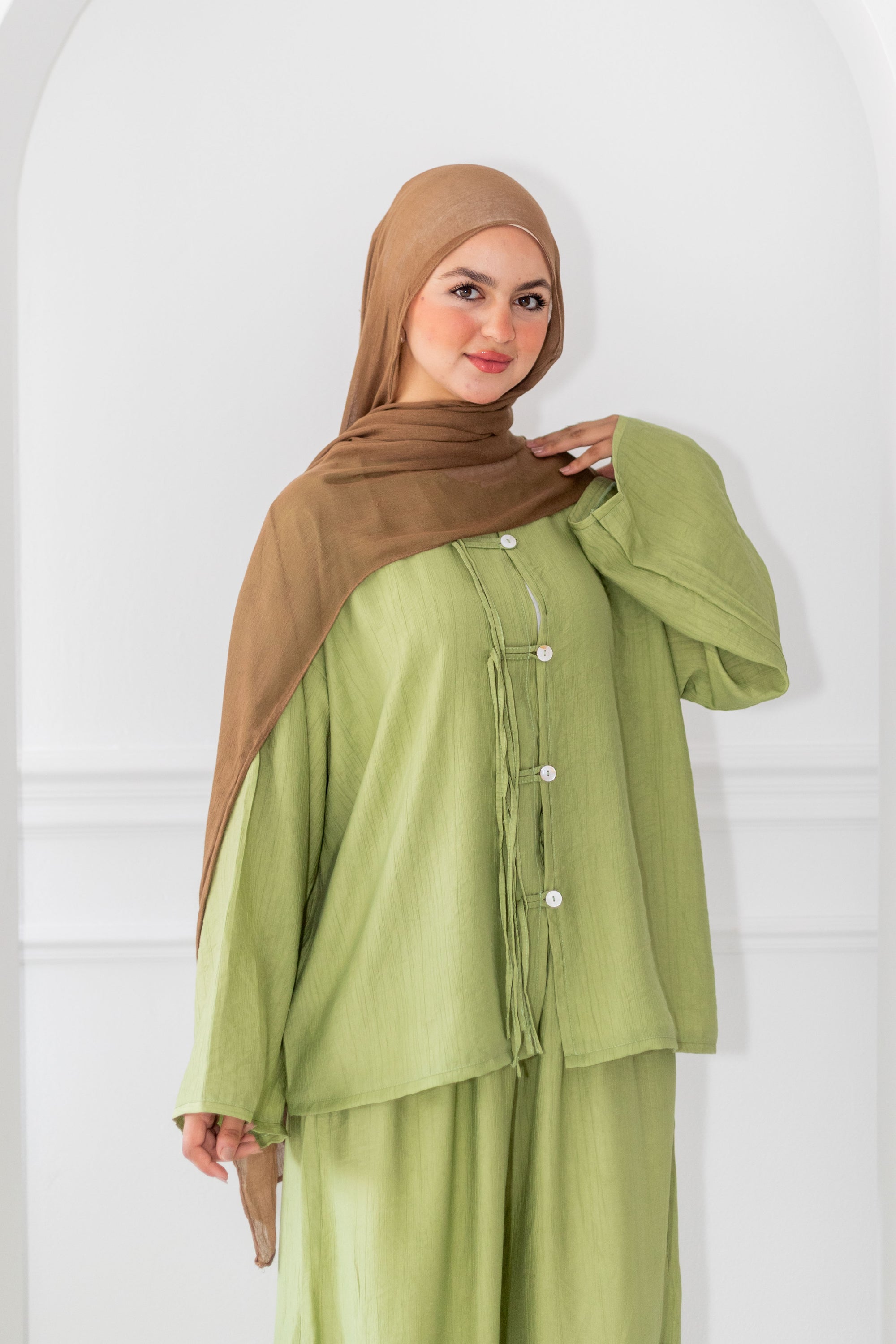Woman wearing a green outfit with a brown hijab against a white background