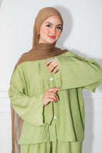 Woman wearing a green outfit with a brown hijab against a white background