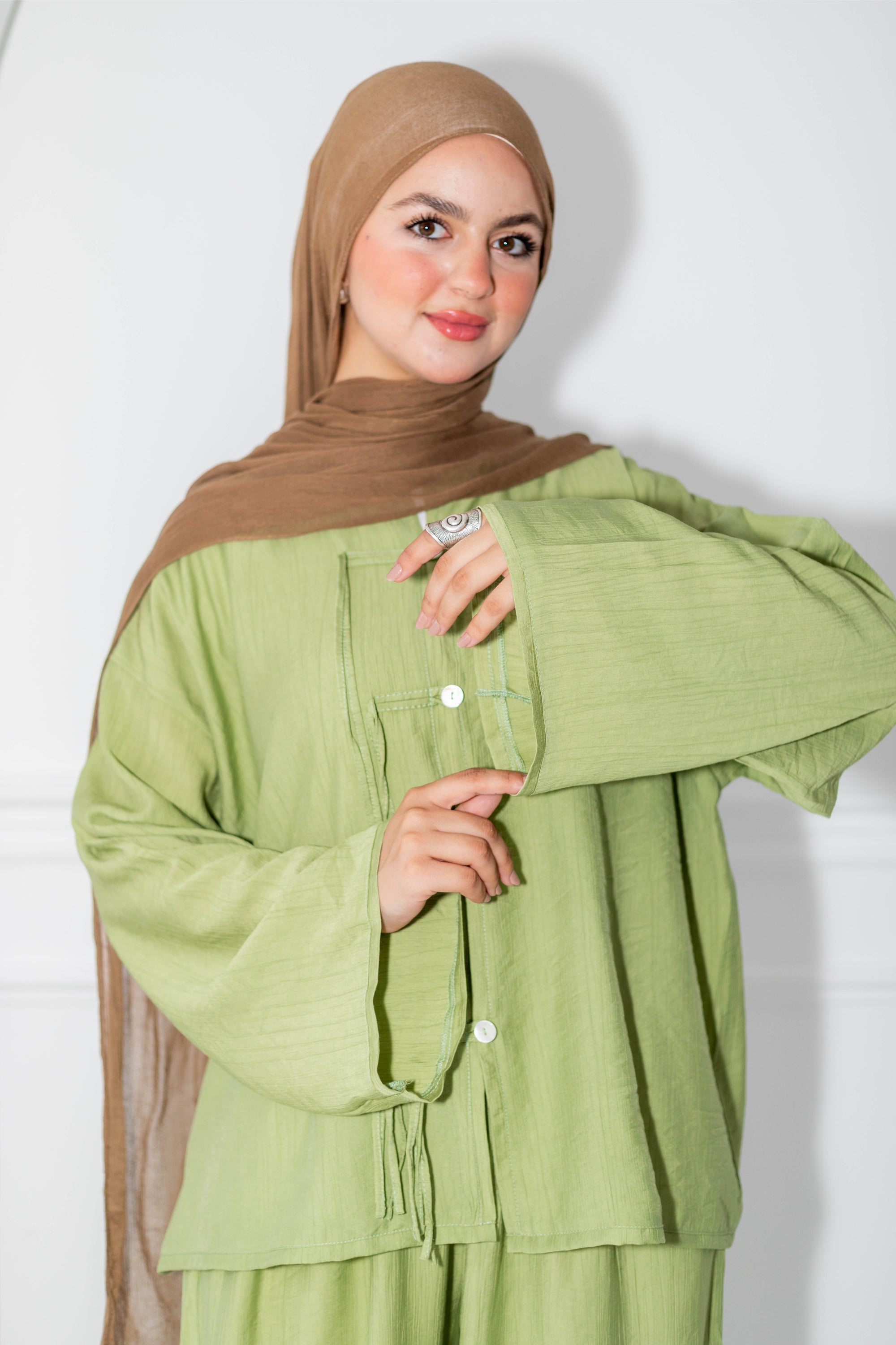 Woman wearing a green outfit with a brown hijab against a white background