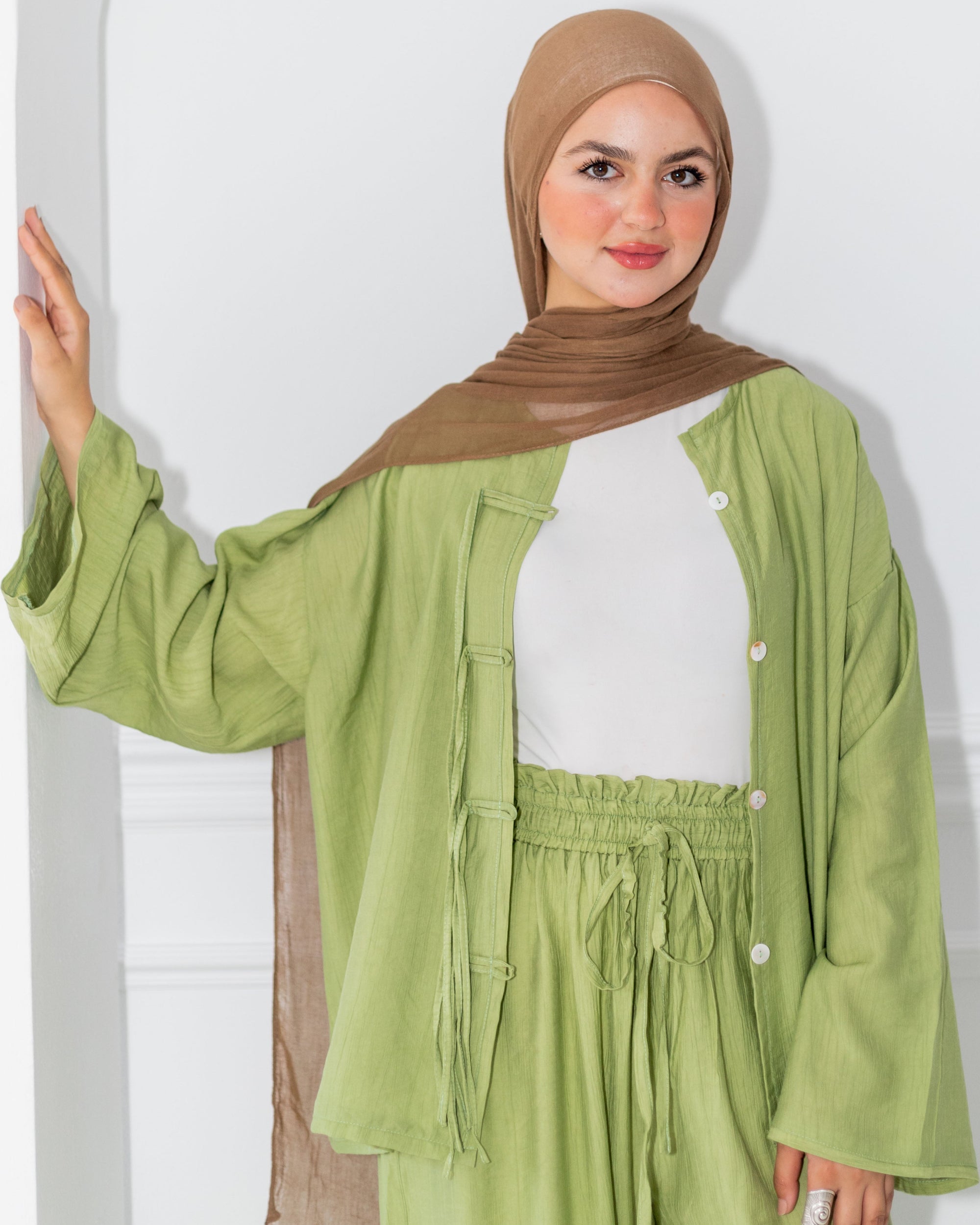 Woman wearing a green outfit with a brown hijab against a white background