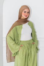 Woman wearing a green outfit with a brown hijab against a white background