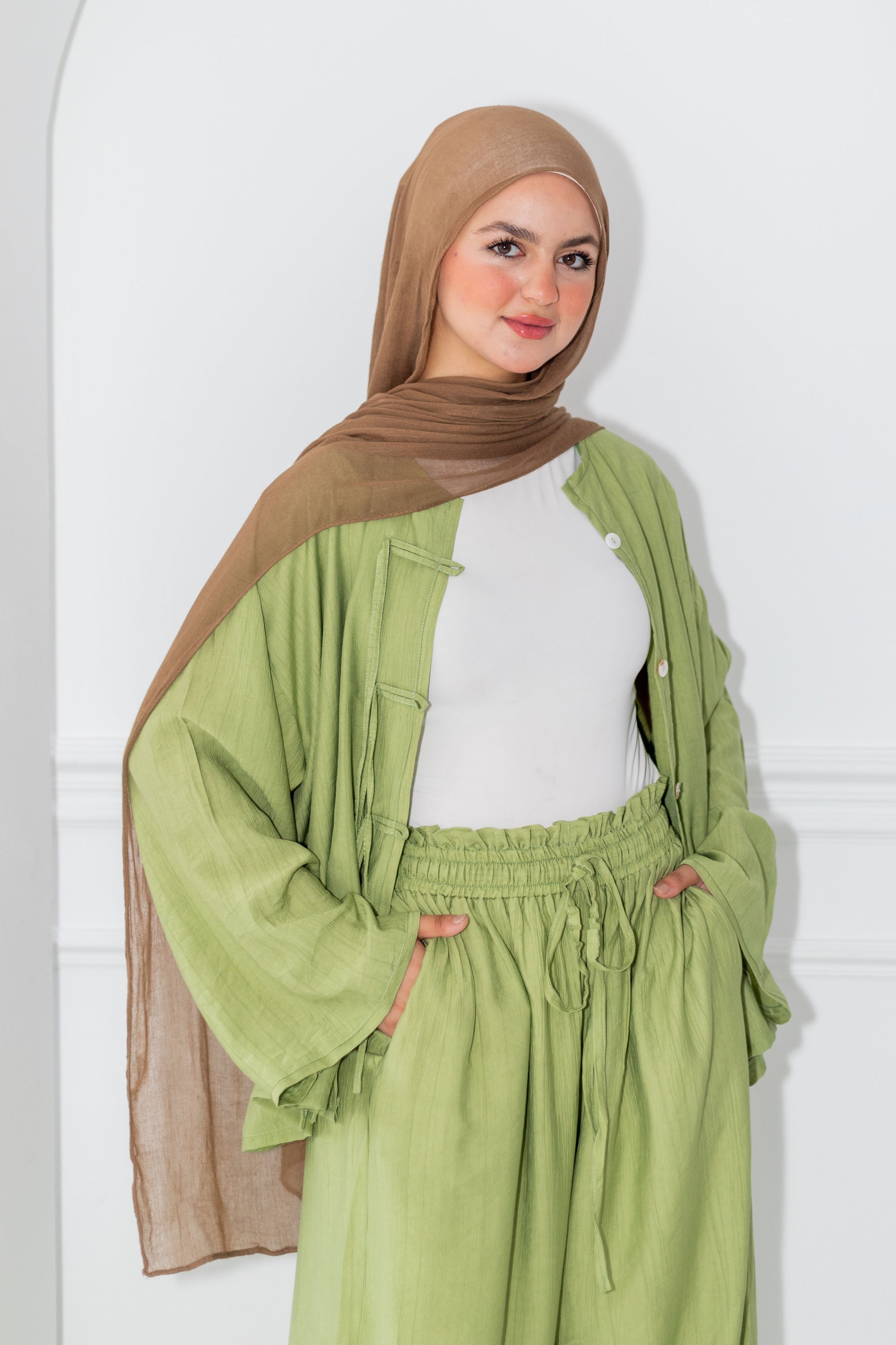 Woman wearing a green outfit with a brown hijab against a white background