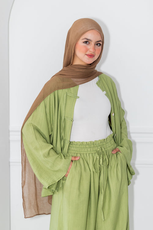 Woman wearing a green outfit with a brown hijab against a white background