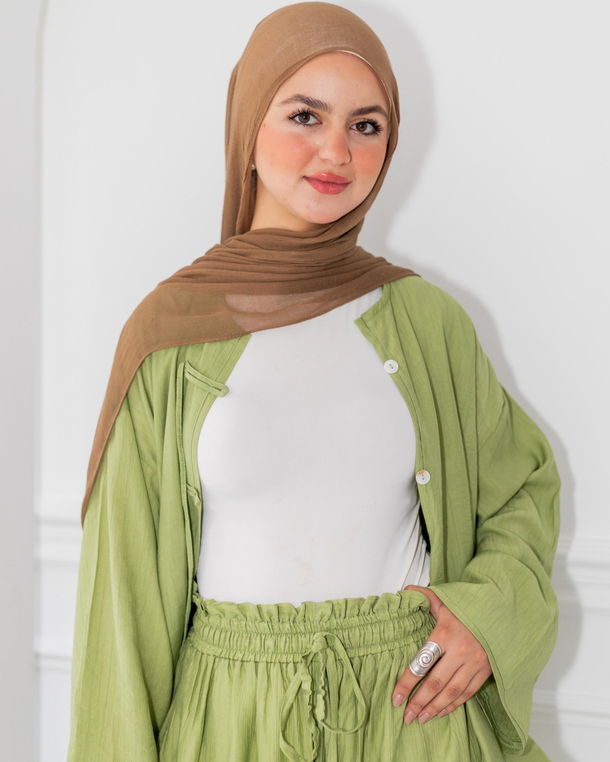 Woman wearing a green outfit with a brown hijab against a white background