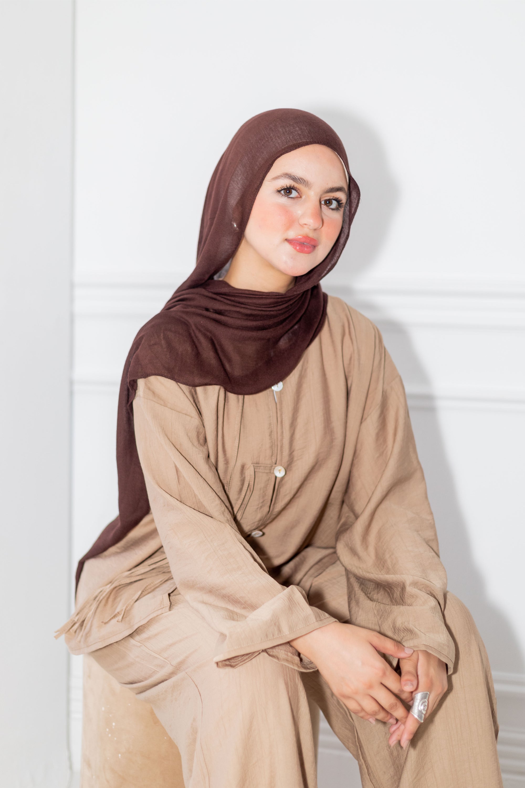 Woman wearing a brown hijab and beige outfit against a white background
