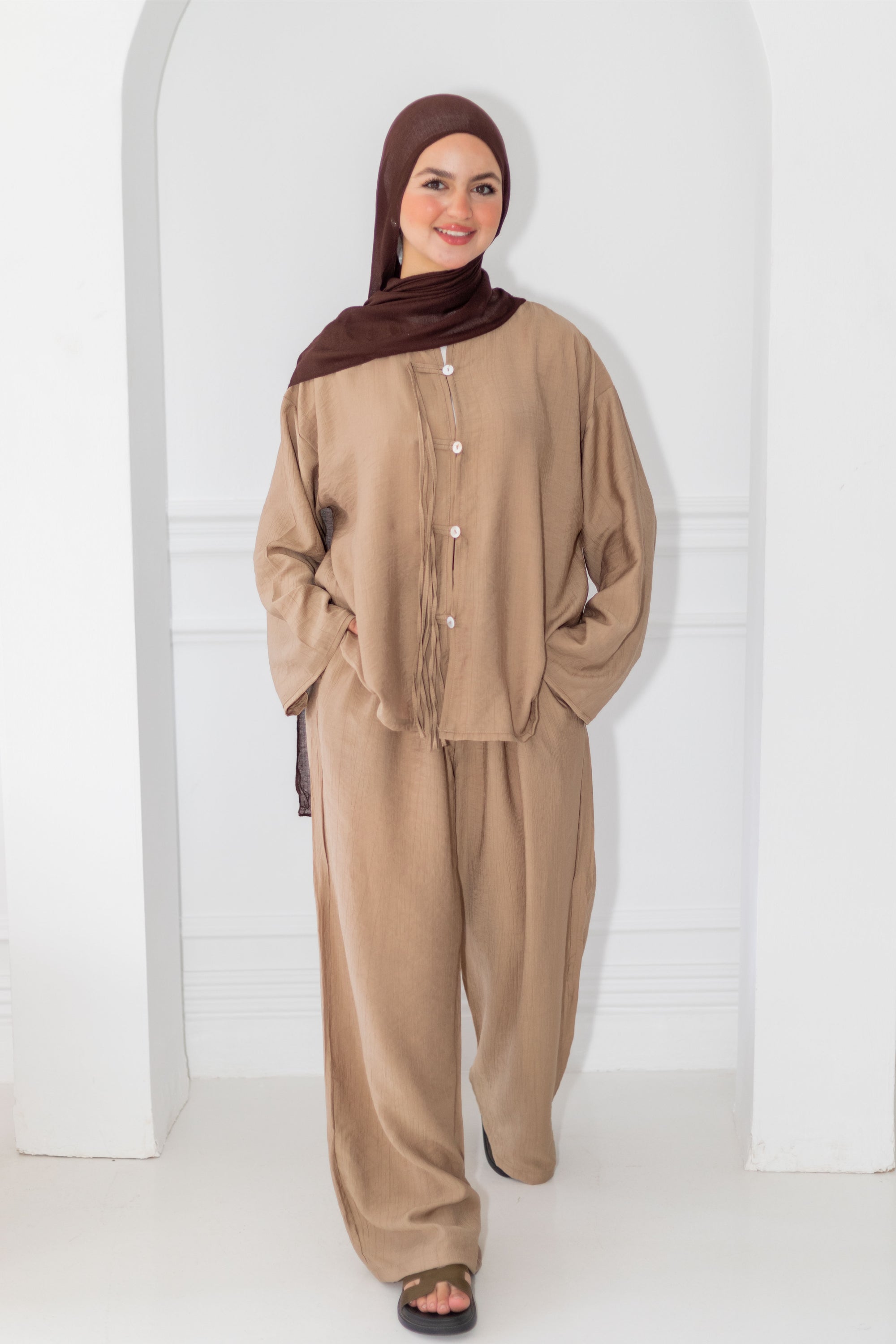 Woman wearing a beige outfit with a brown hijab against a white background