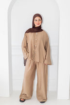 Woman wearing a beige outfit with a brown hijab against a white background