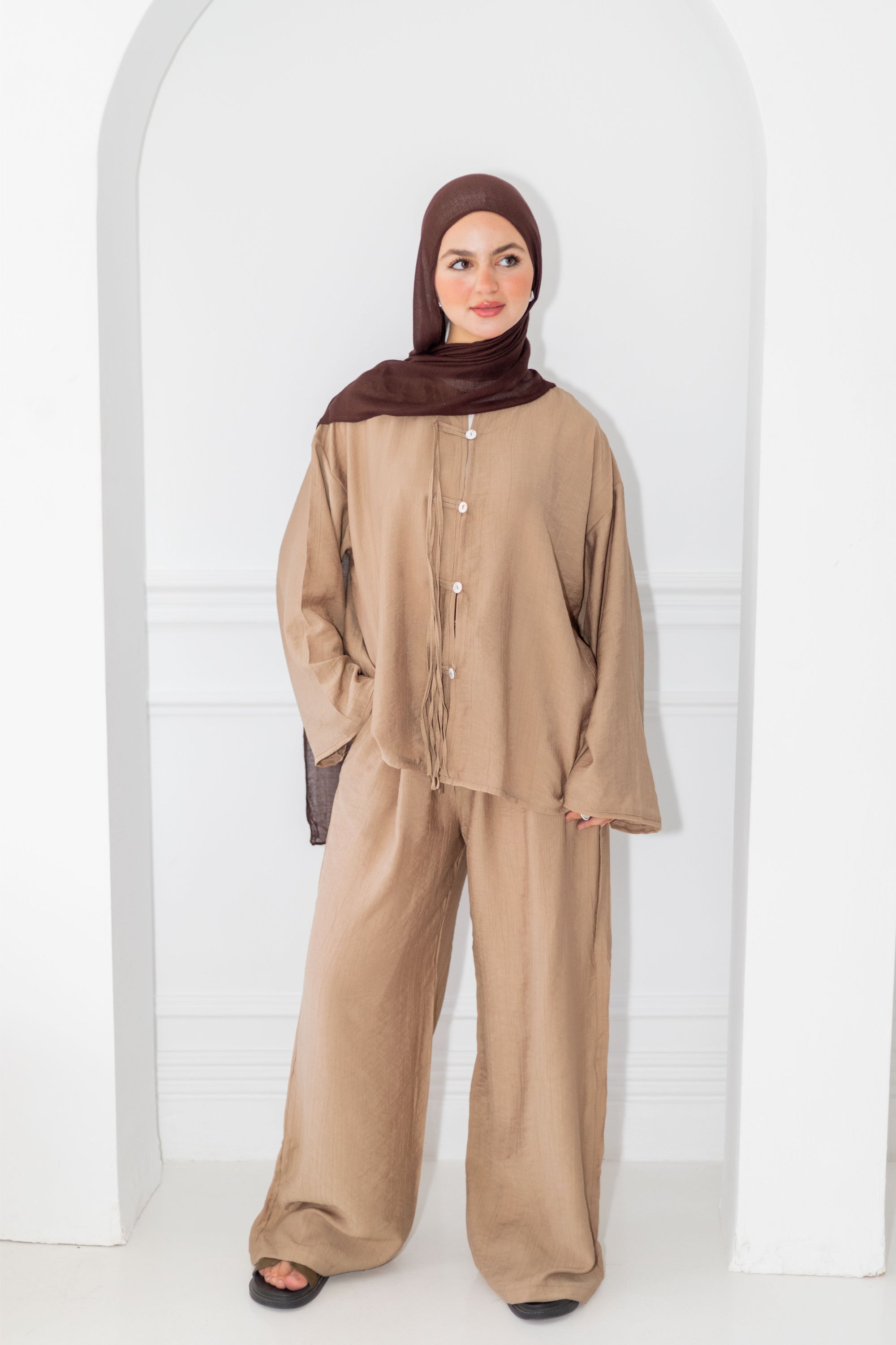 Woman wearing a beige outfit with a brown hijab against a white background