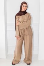 Woman wearing a beige outfit with a brown hijab against a white background