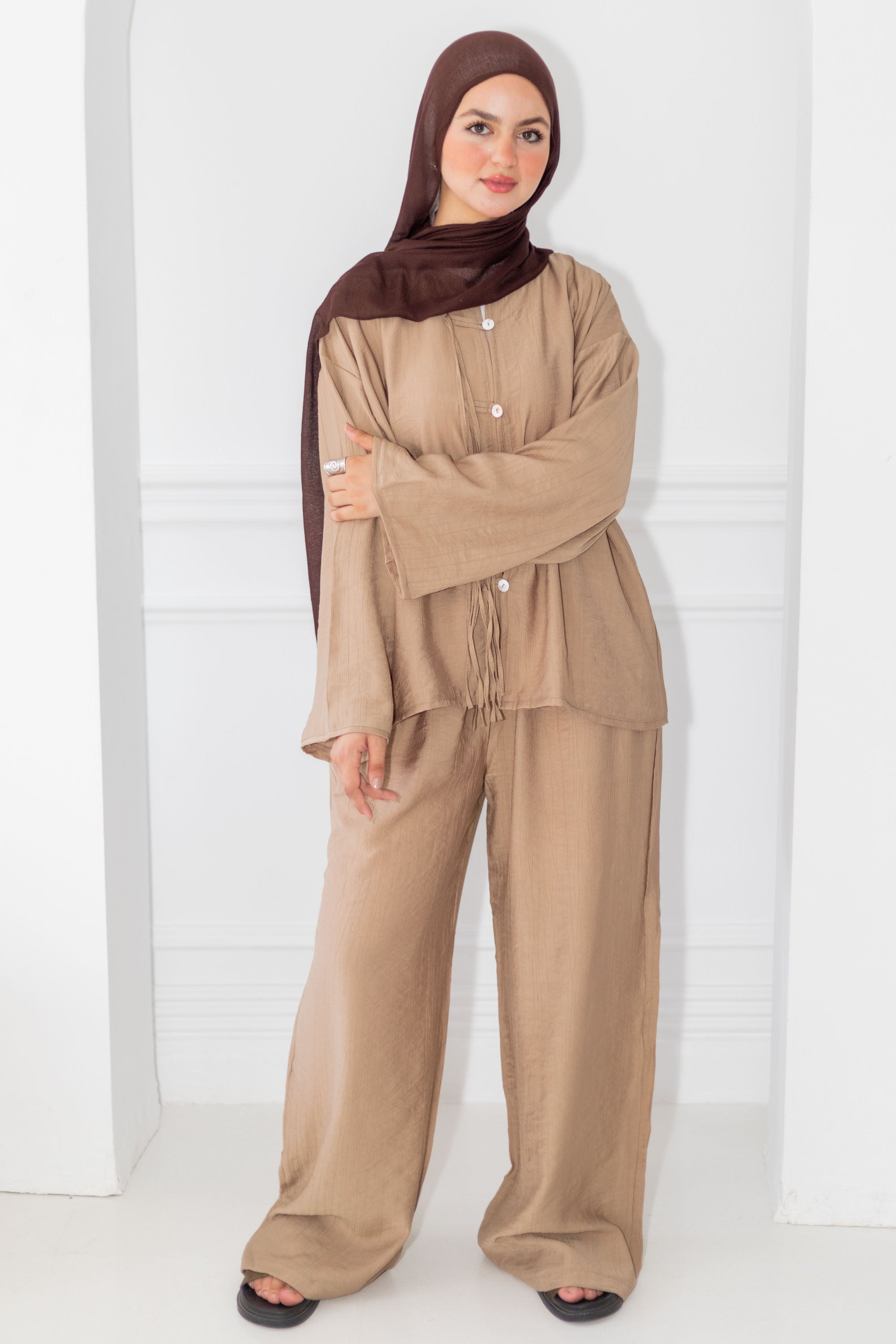 Woman wearing a beige outfit with a brown hijab against a white background
