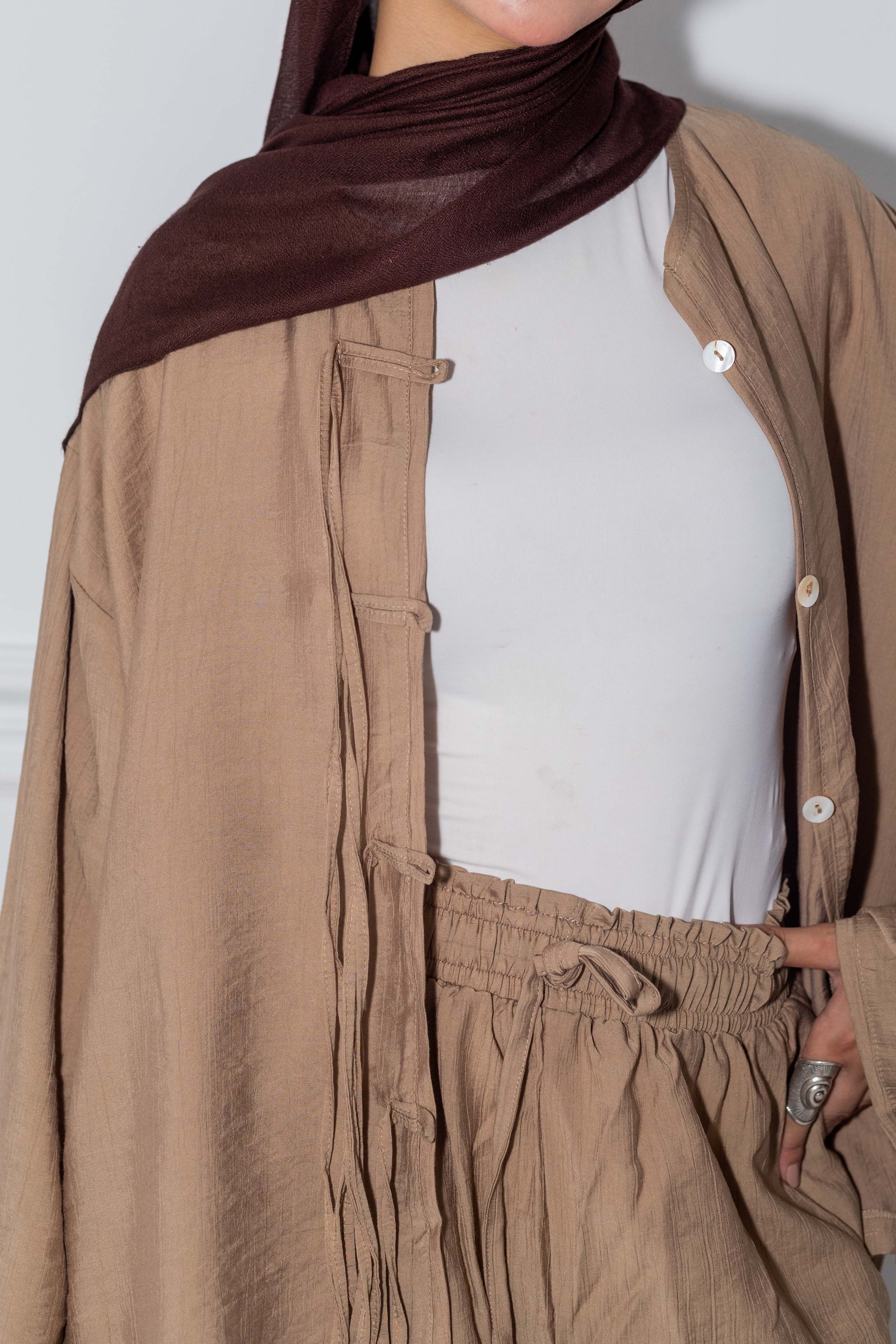 Person wearing a brown outfit with a white shirt underneath on a plain background