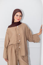 Woman wearing a beige outfit with a brown hijab against a white background