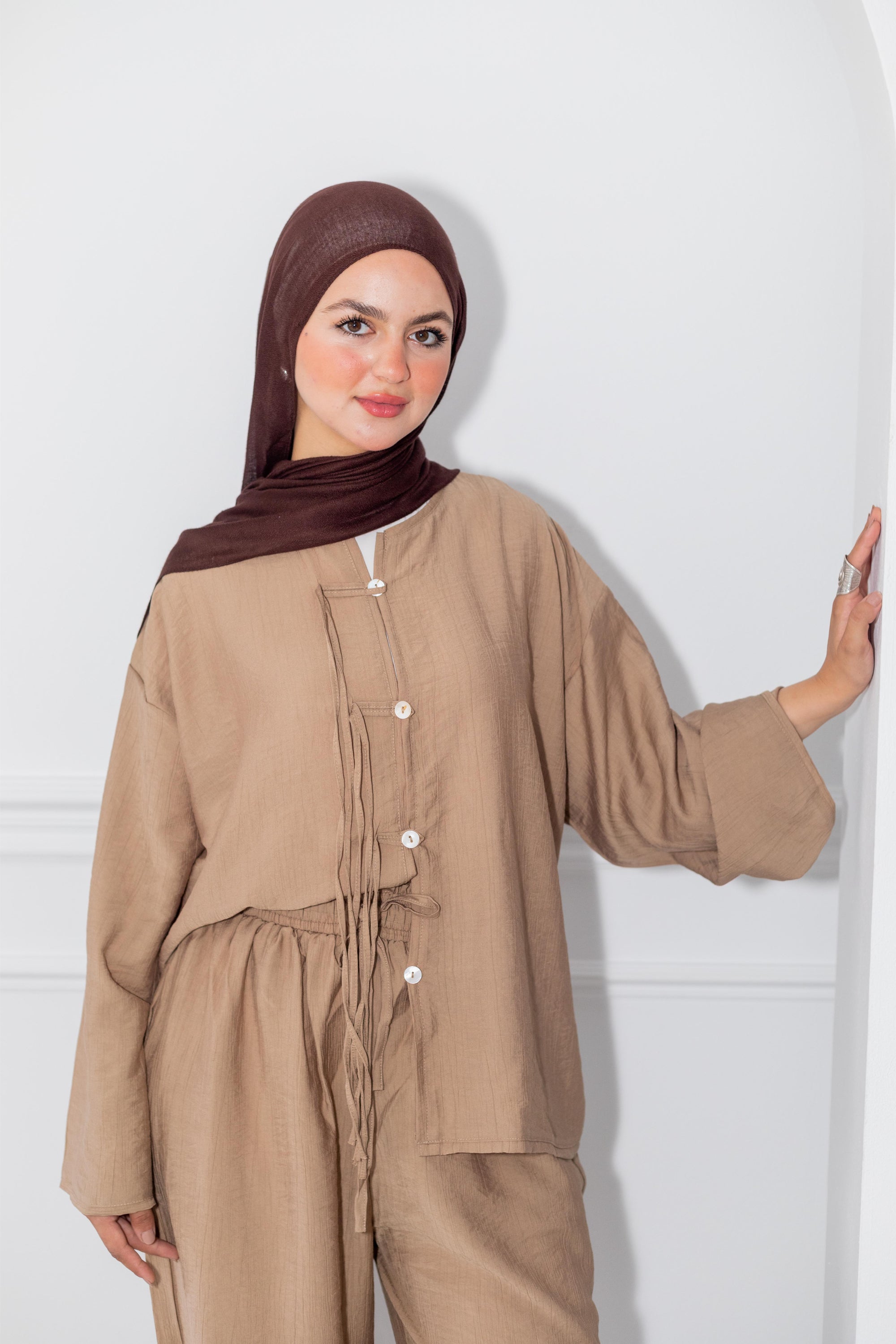 Woman wearing a beige outfit with a brown hijab against a white background