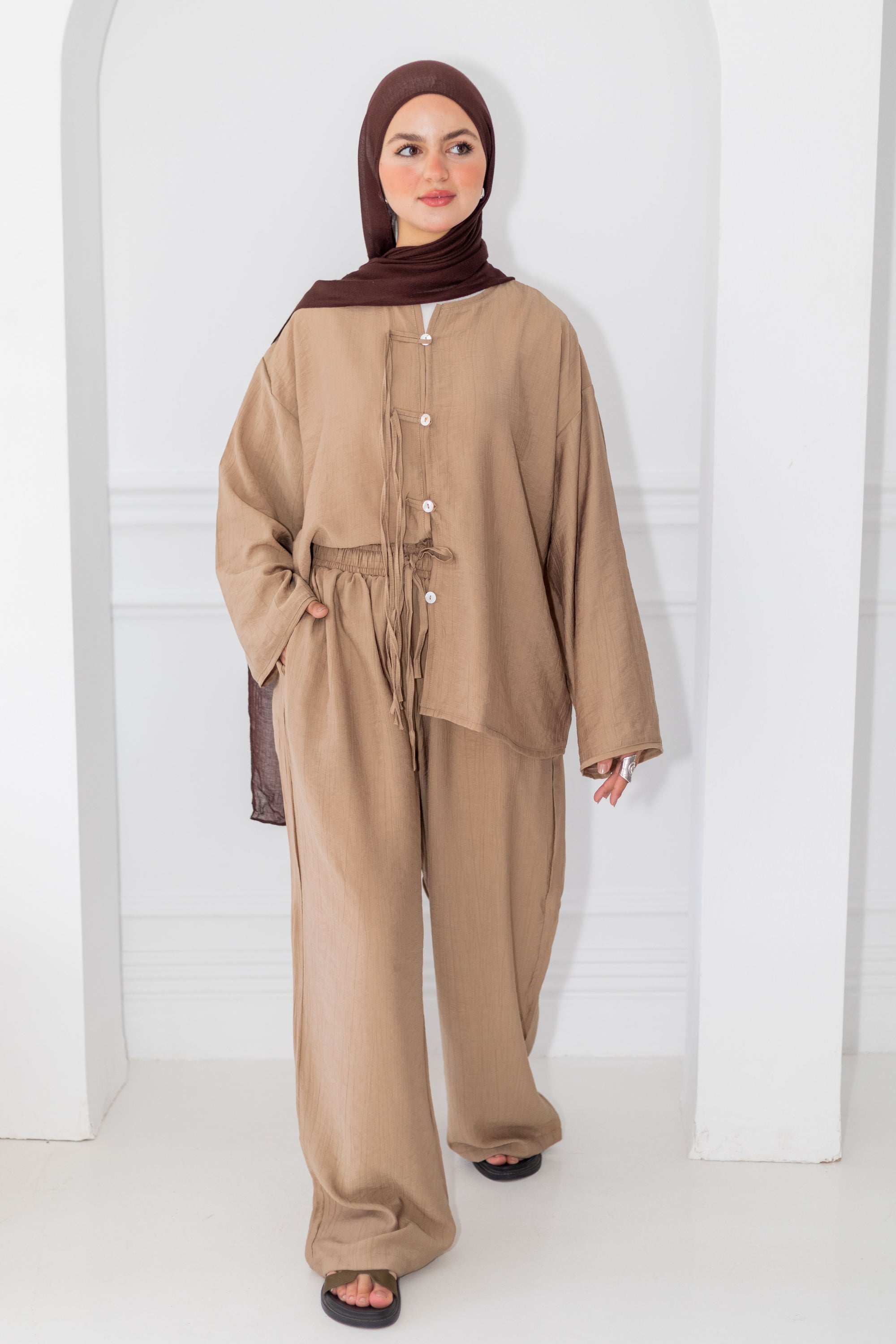Woman wearing a beige outfit with a hijab against a white background
