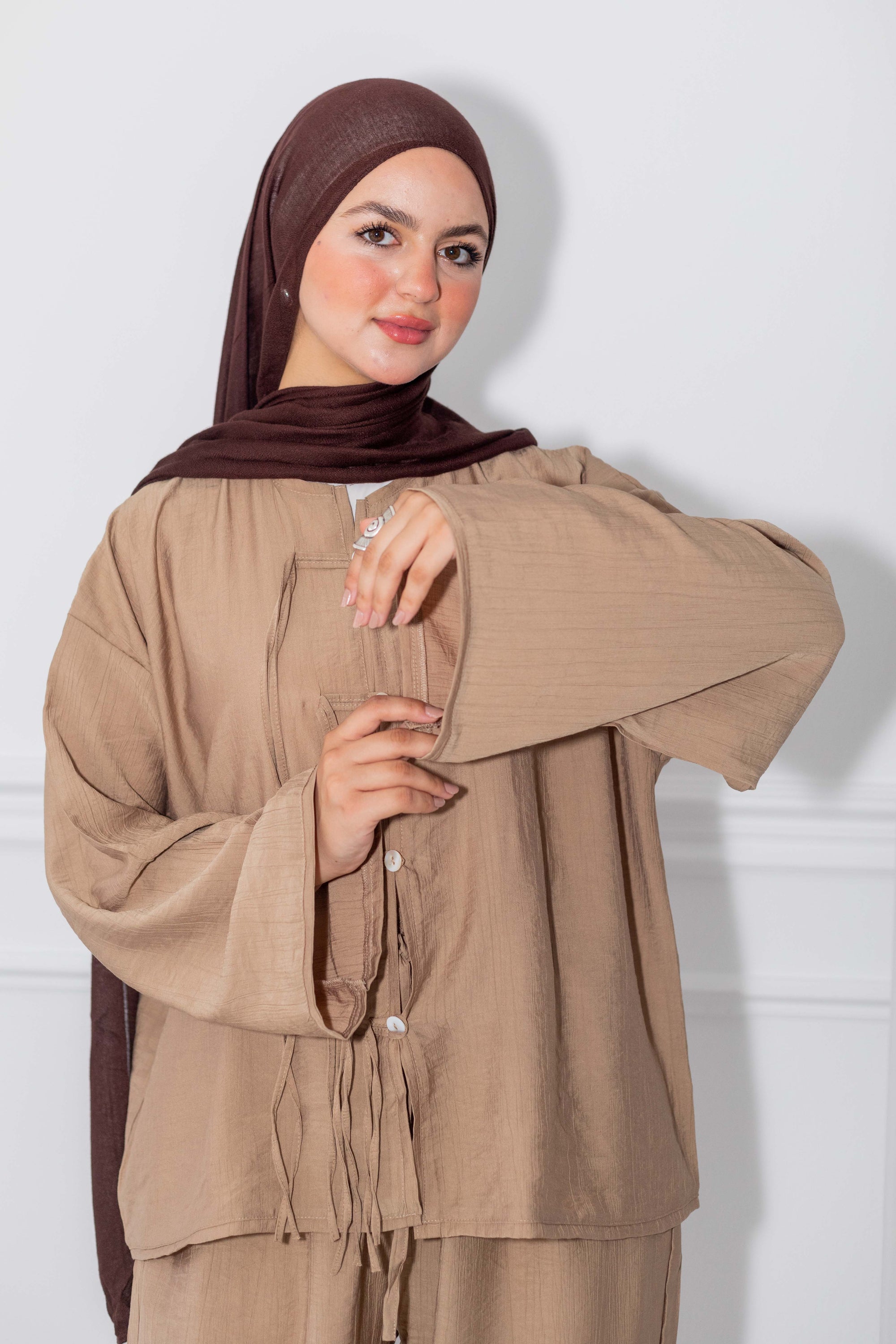 Woman wearing a brown hijab and matching outfit against a white background