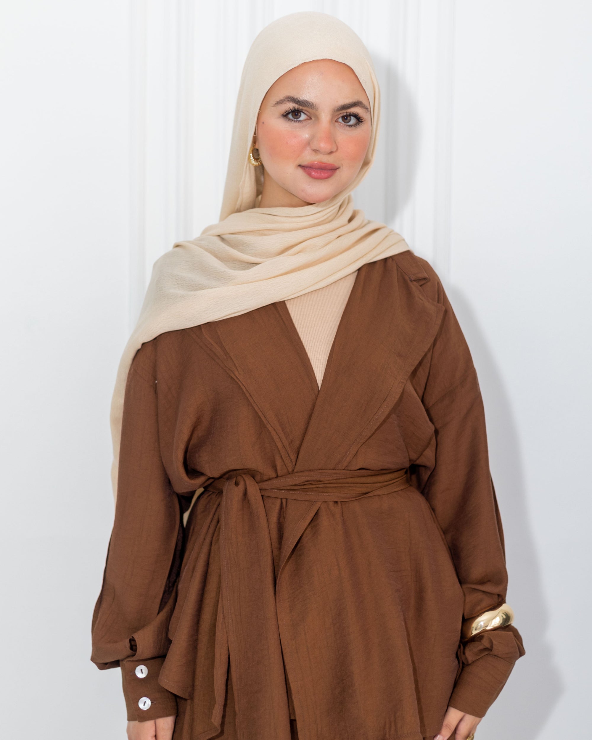 Woman wearing a brown outfit with a beige hijab against a white background