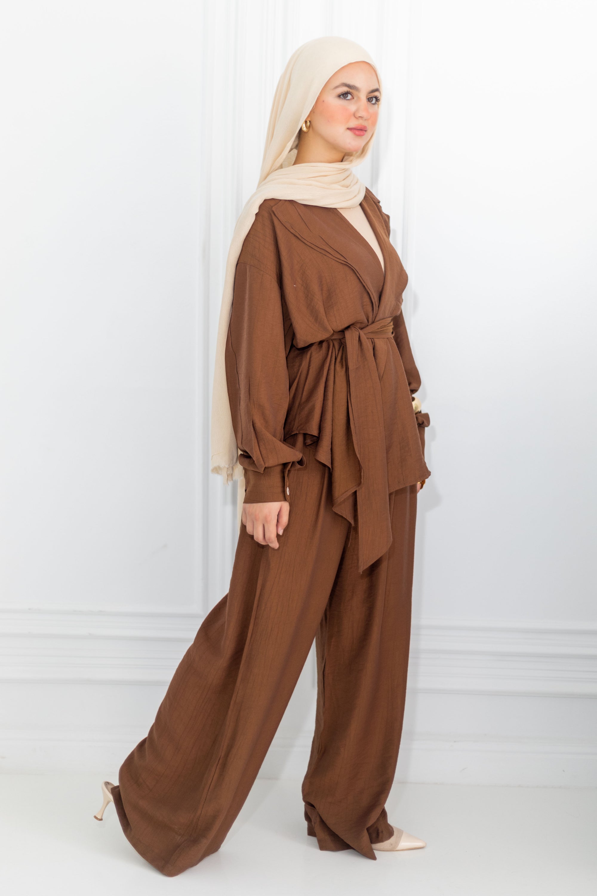 Woman wearing a brown outfit with a beige hijab on a white background