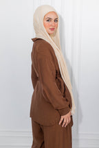 Woman wearing a brown outfit with a beige hijab against a white background