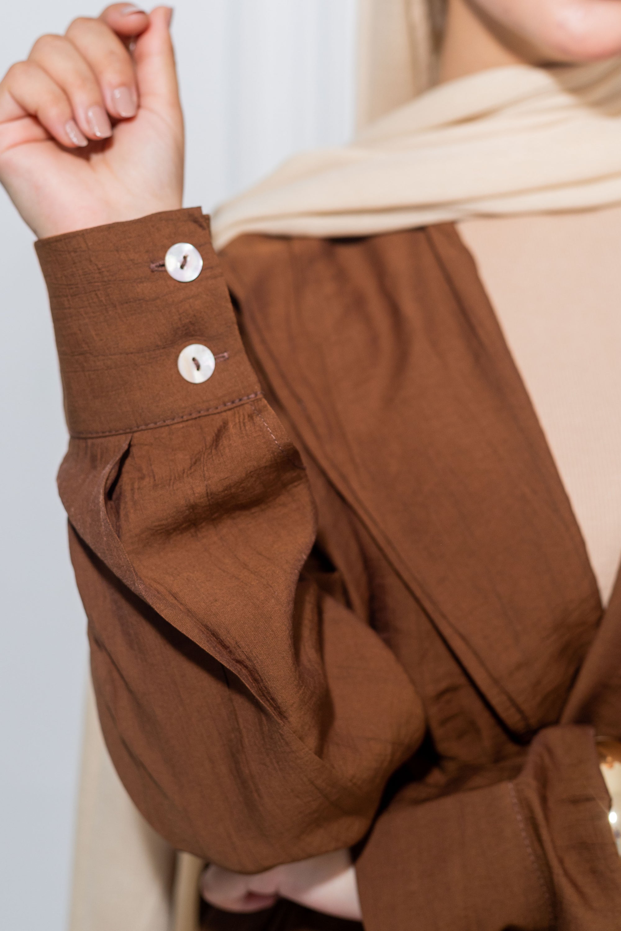 Close-up of a brown jacket with white buttons on a plain background