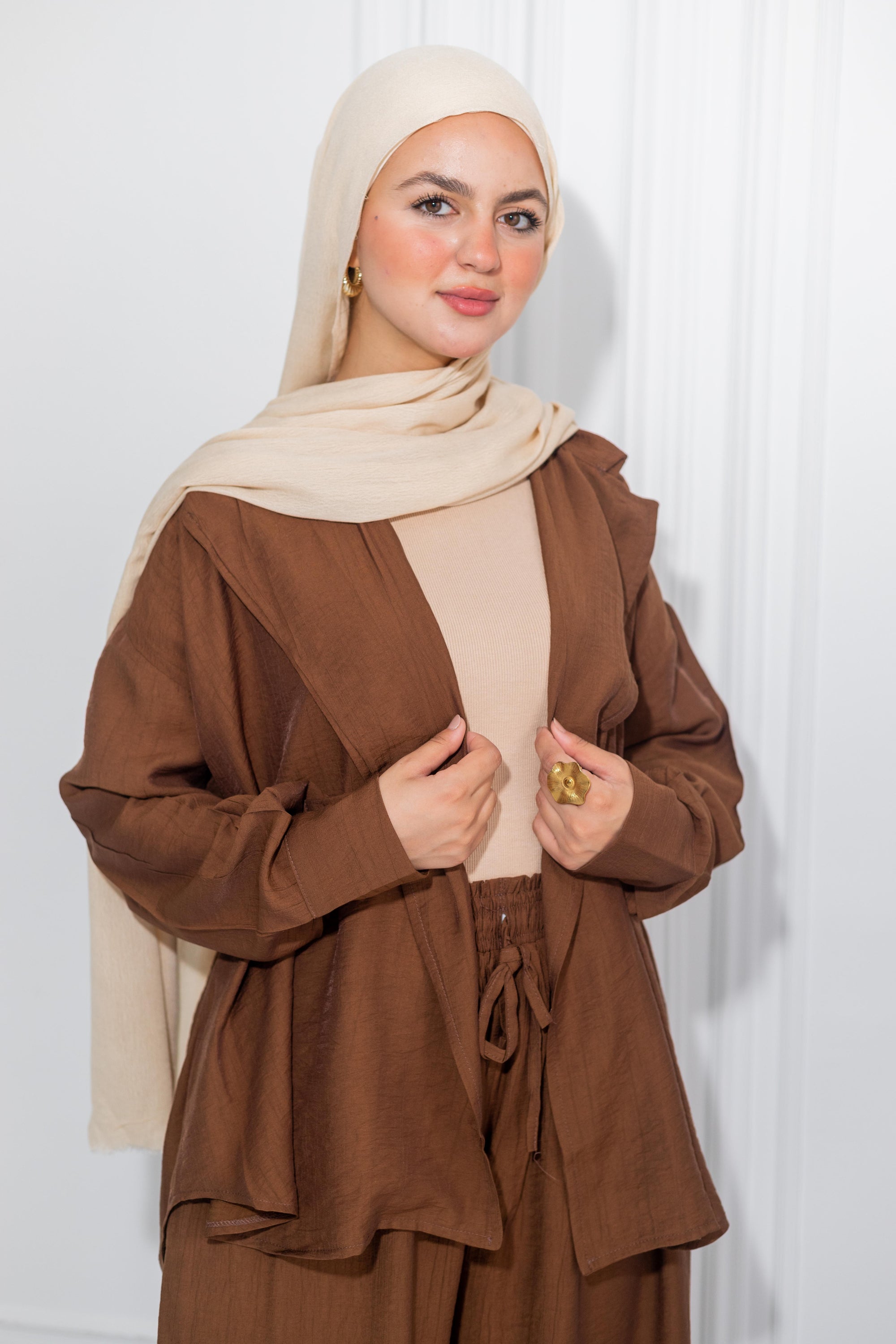 Woman wearing a brown outfit with a beige hijab against a white background