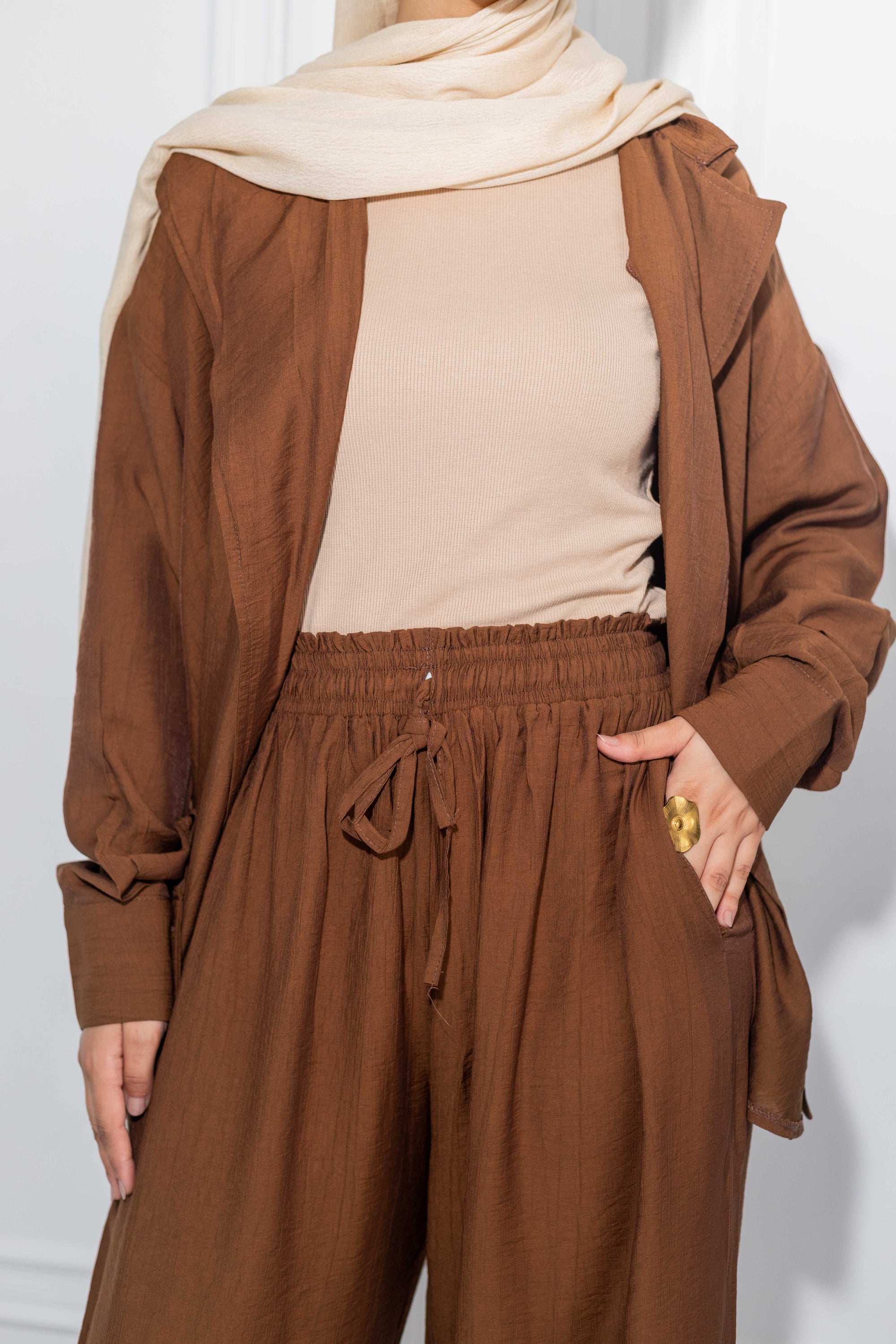 Person wearing a brown outfit with a beige hijab against a white background