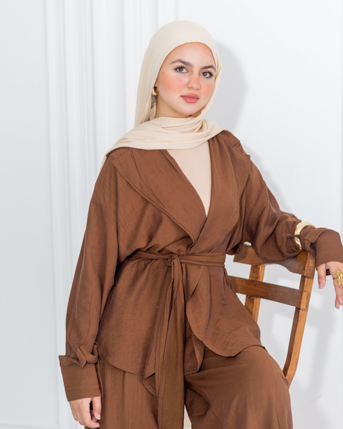 Woman wearing a brown outfit with a beige hijab sitting on a chair against a white background