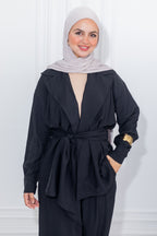 Woman wearing a black outfit with a light gray hijab against a white background