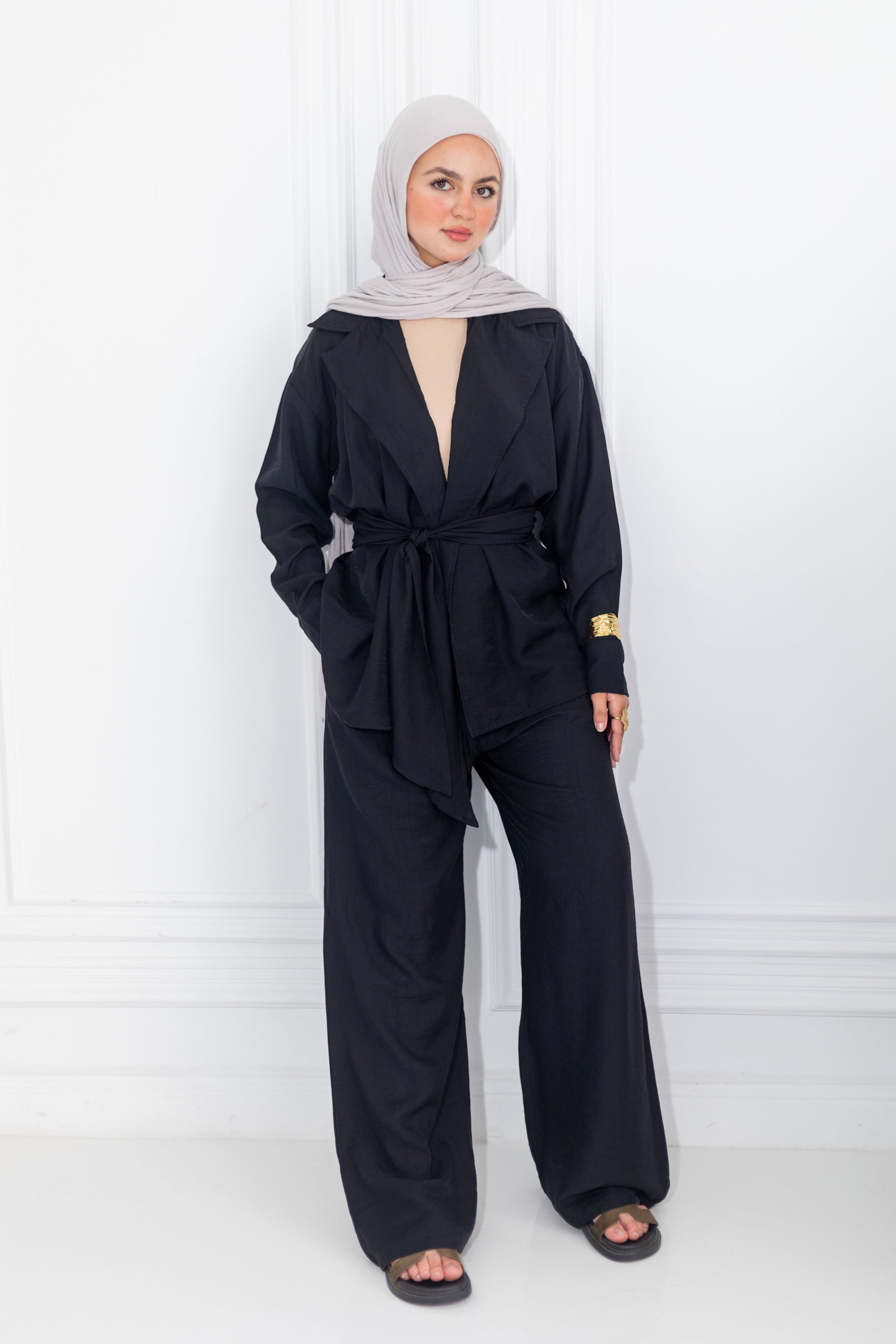 Woman wearing a black outfit with a hijab against a white background