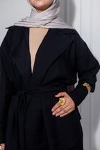 Person wearing a black outfit with a gold ring, standing against a plain background