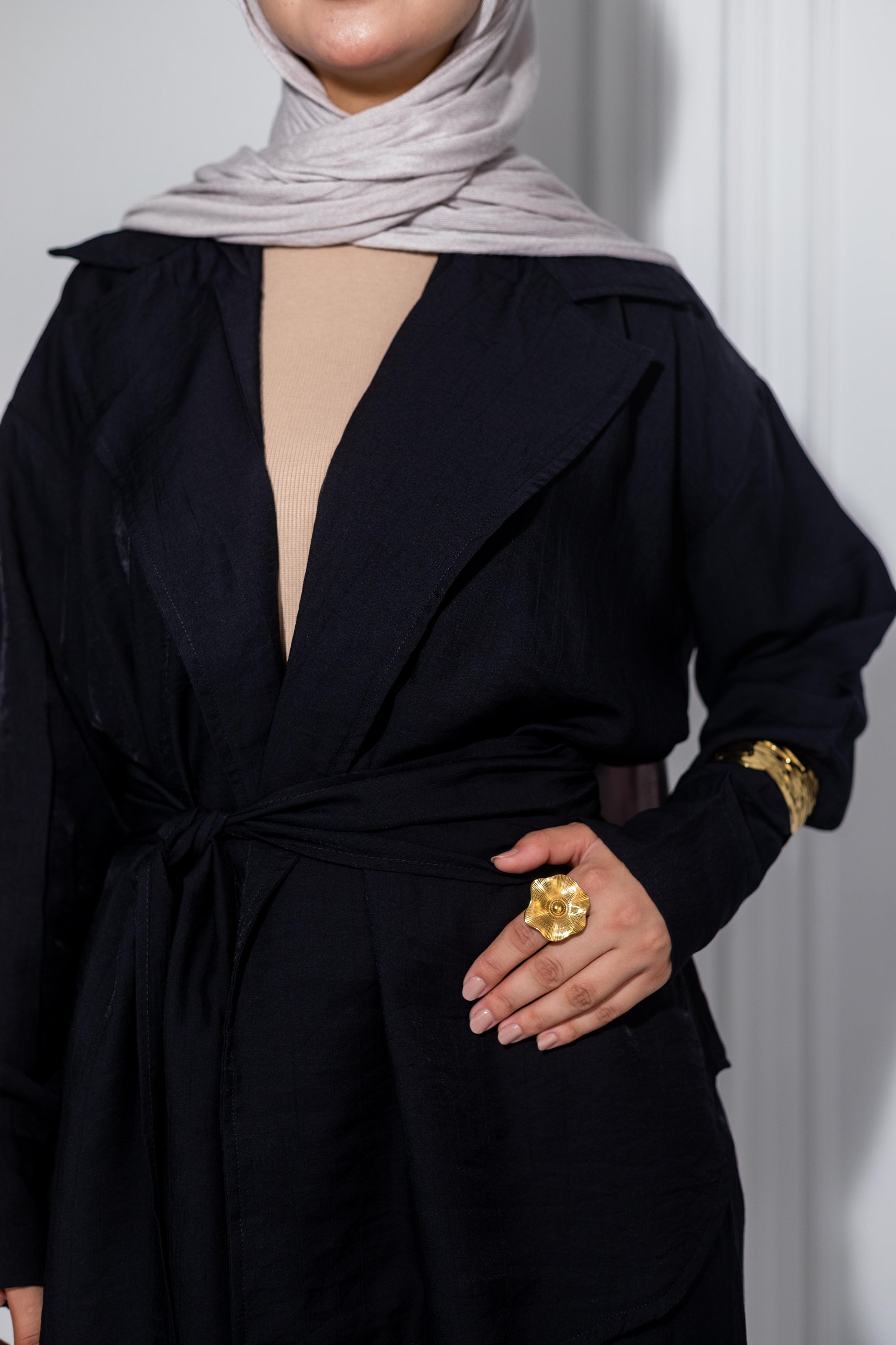 Person wearing a black outfit with a gold ring, standing against a plain background
