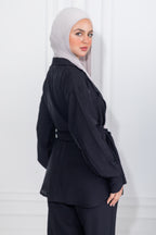 Woman wearing a black outfit with a light gray hijab against a white background