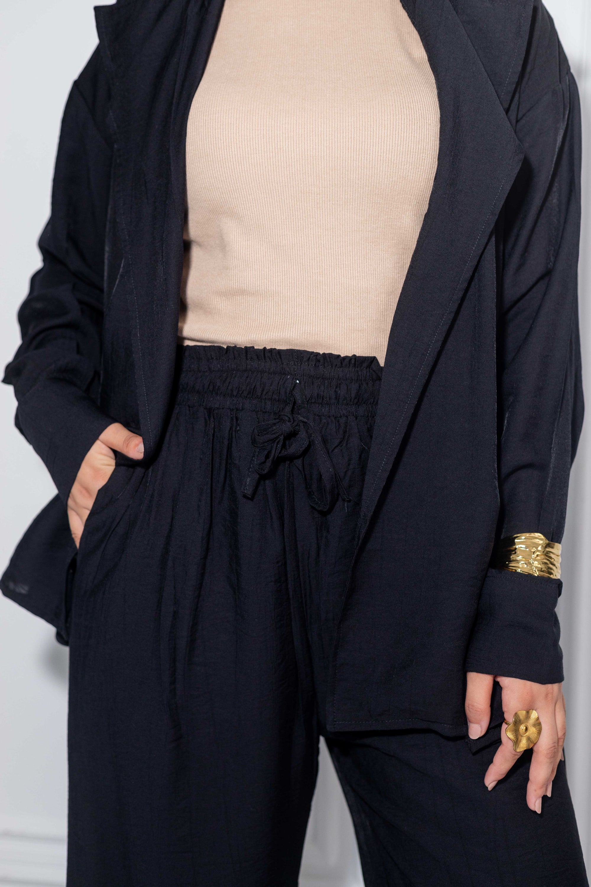 Person wearing a black outfit with a beige top, standing against a white background