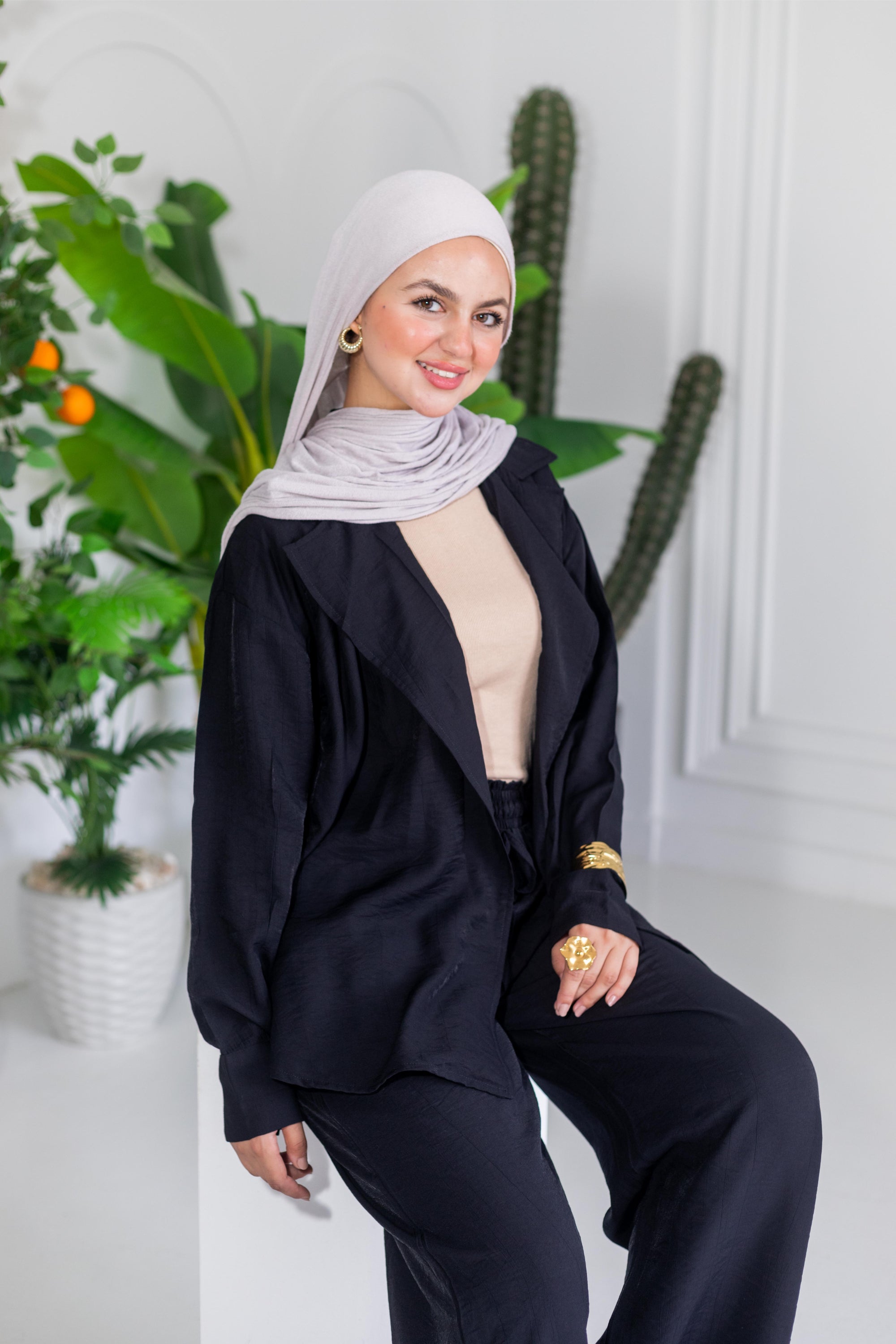 Woman wearing a black outfit with a white hijab in a room with plants.