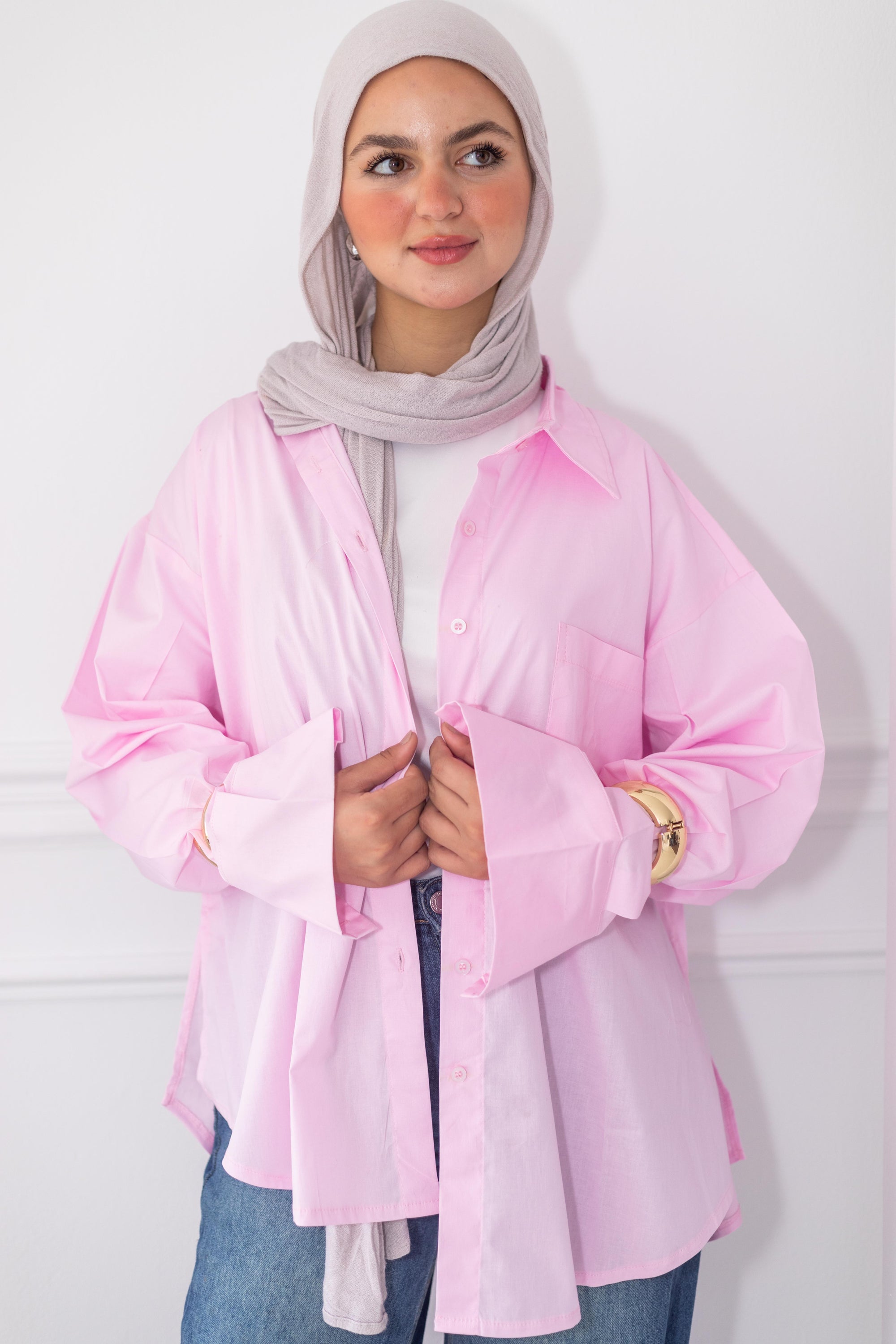 Woman wearing a pink shirt and gray hijab against a white background