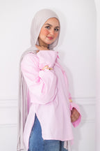 Woman wearing a light pink hijab and blouse with blue jeans against a white background