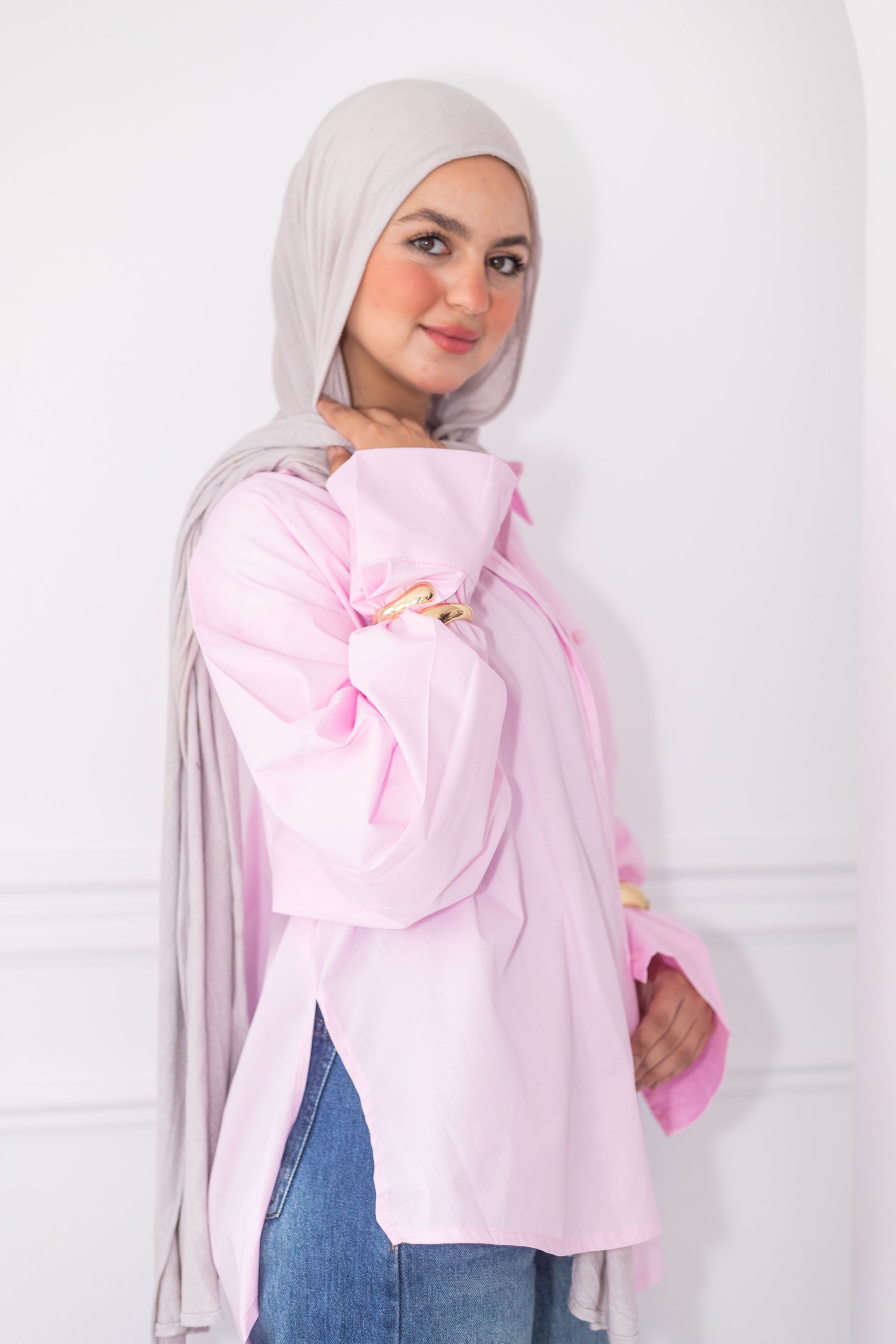 Woman wearing a light pink hijab and blouse with blue jeans against a white background