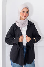 Woman wearing a black jacket, white top, and blue jeans with a light gray hijab against a white background