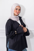 Woman wearing a black jacket and light gray hijab against a white background
