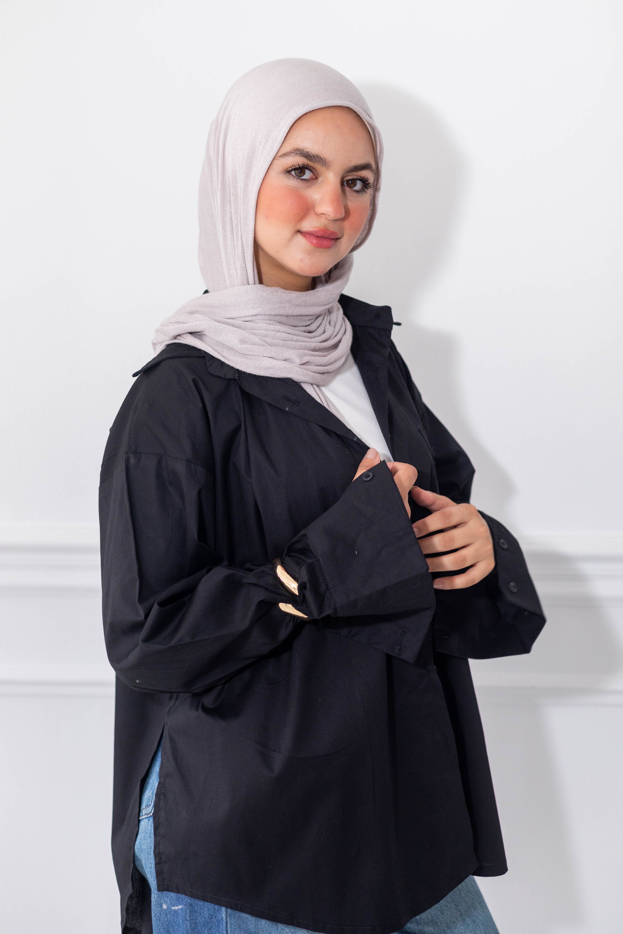 Woman wearing a black jacket and light gray hijab against a white background