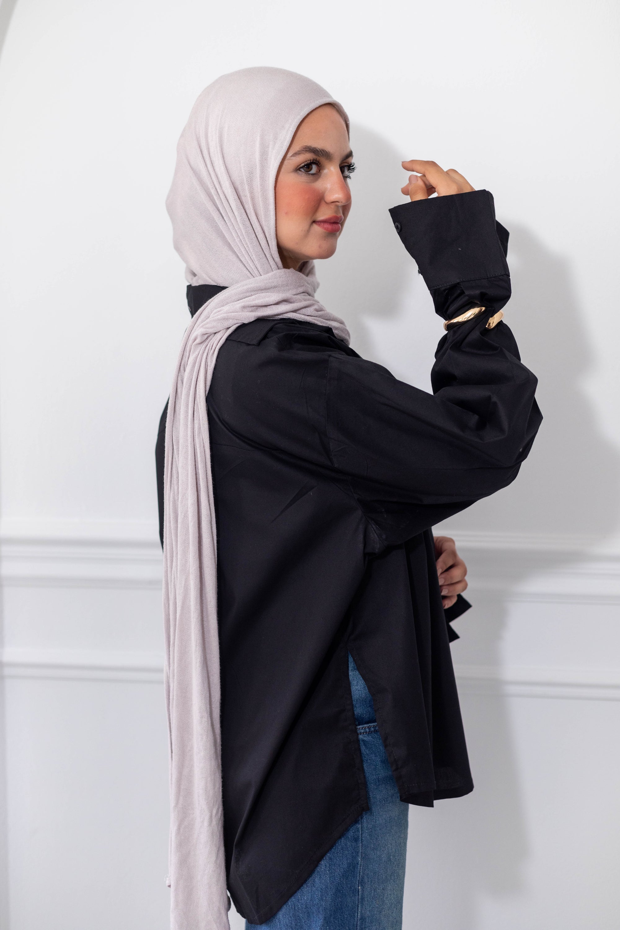 Woman wearing a black outfit with a light pink hijab against a white background