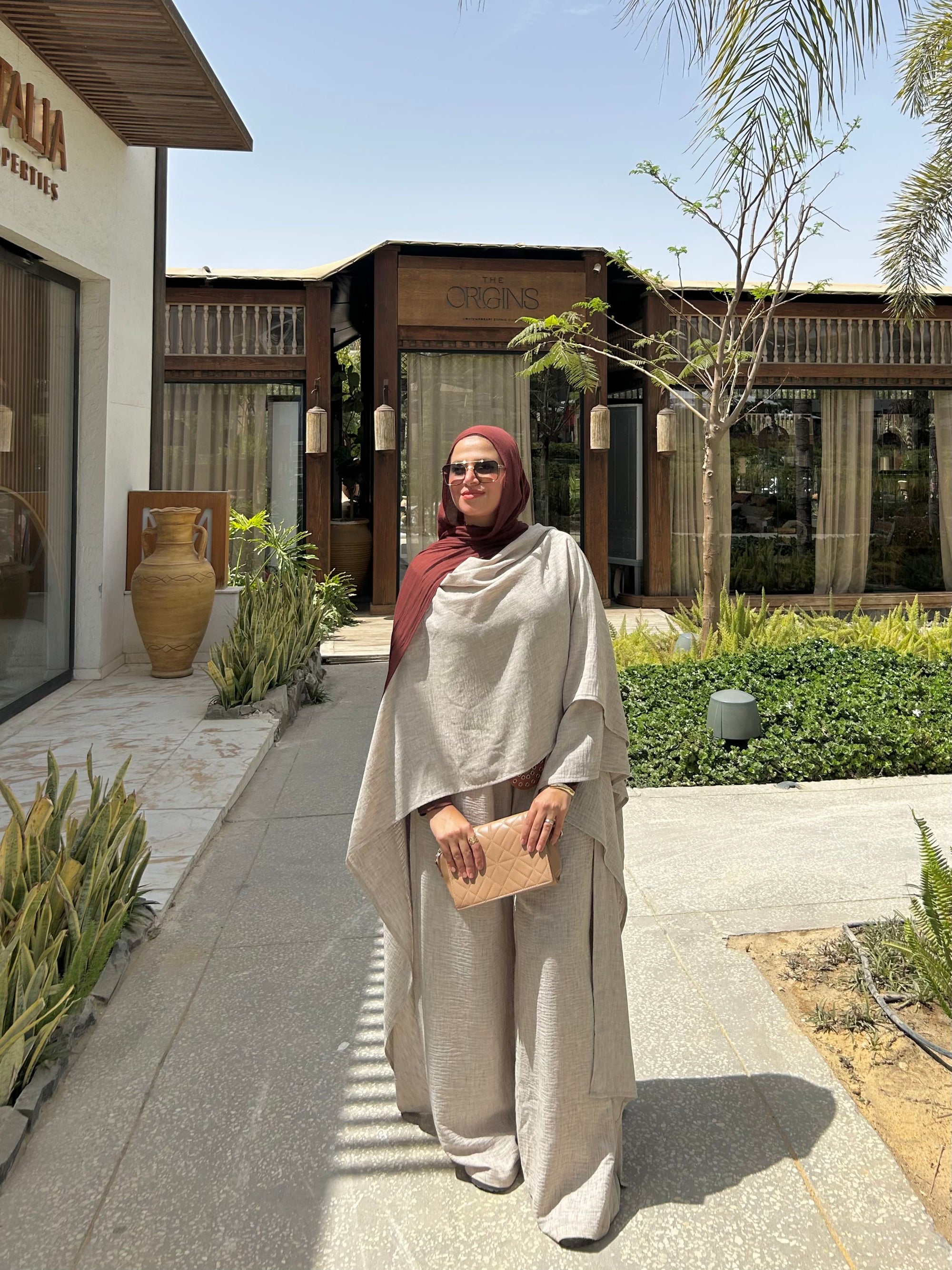 Woman in a beige outfit standing in front of a building with 'Alia' branding.