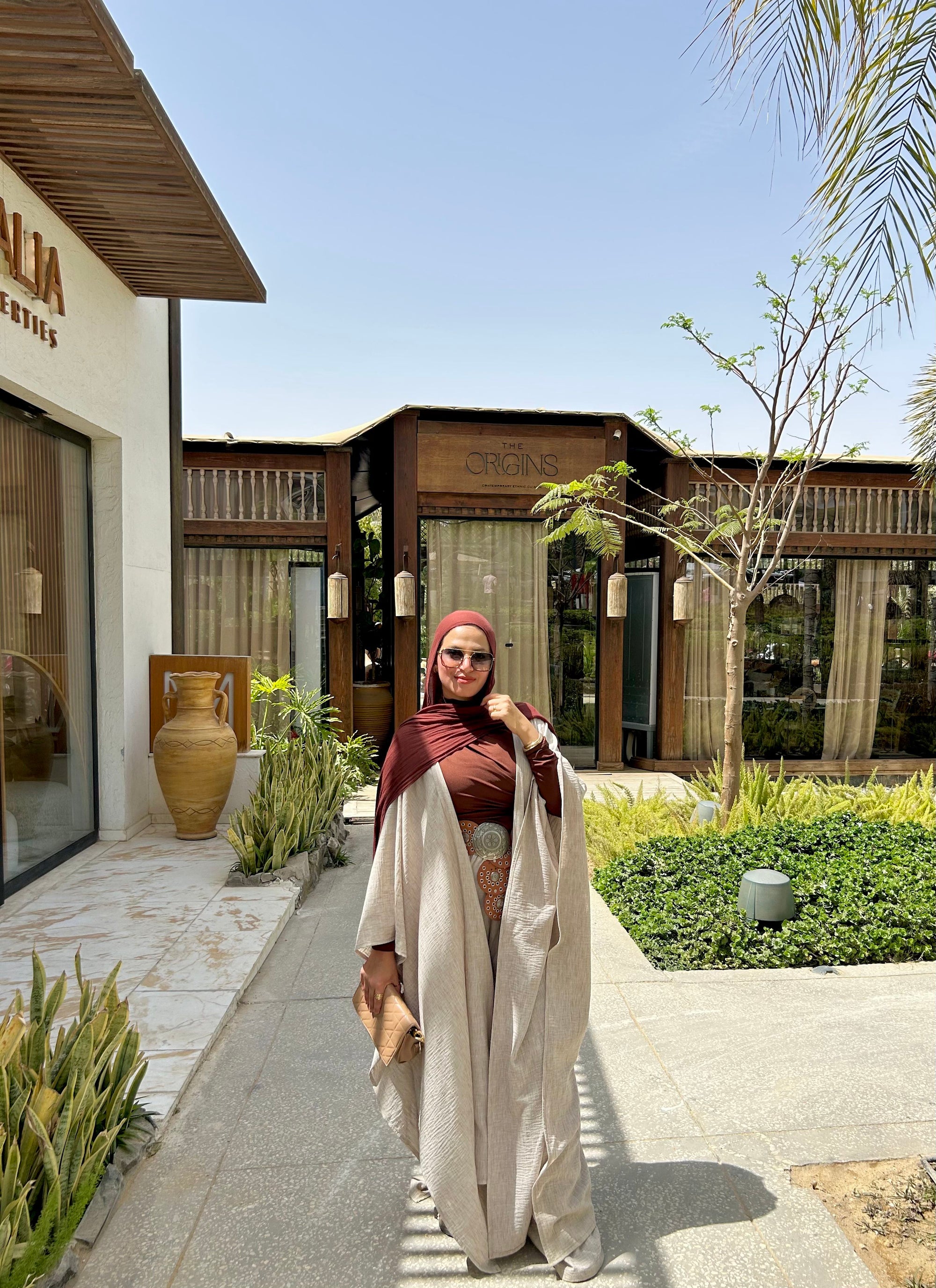 Woman in a red headscarf and white dress standing in front of a building with 'Alila' branding.